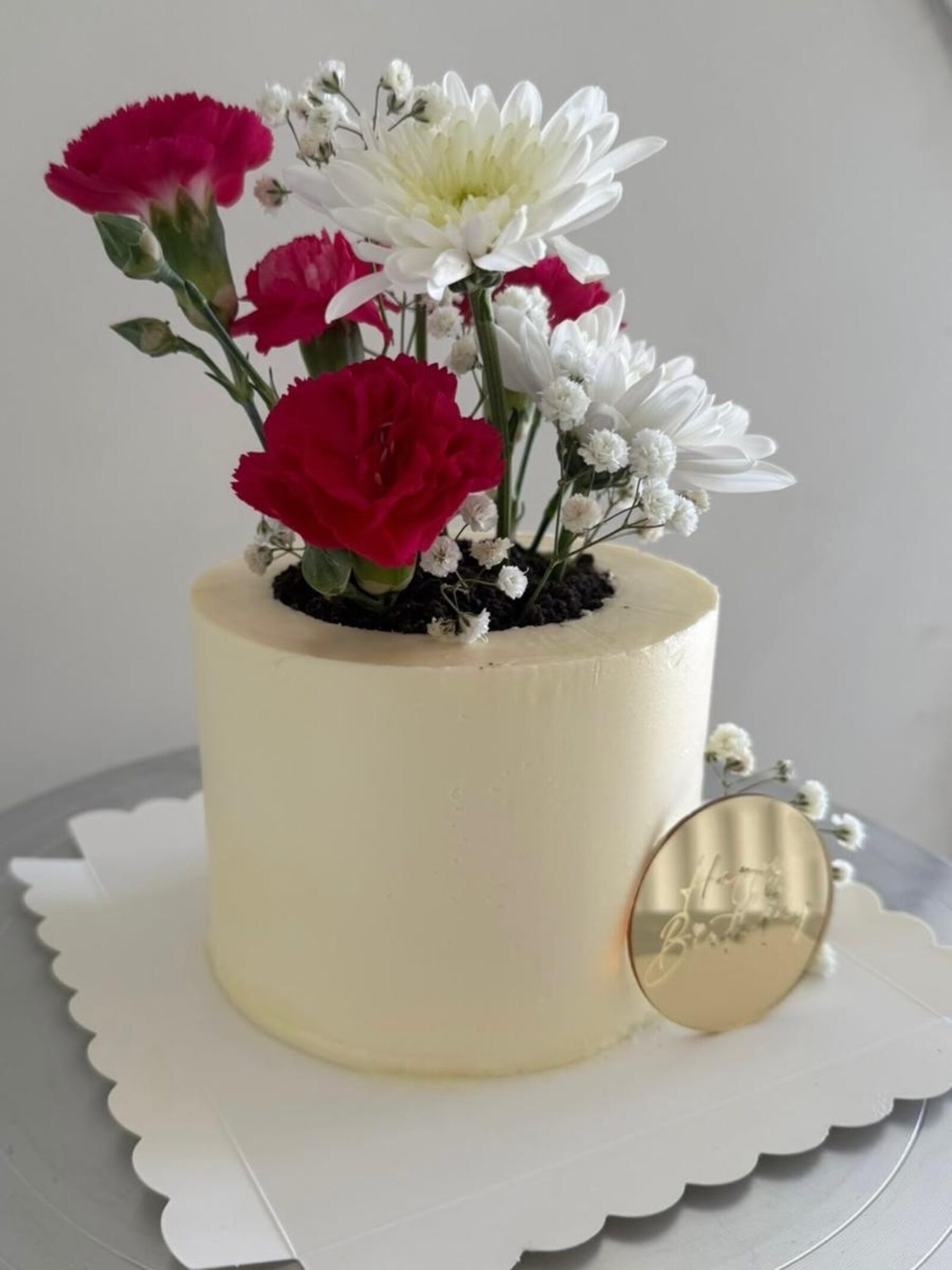 White celebration cake topped with fresh carnations and daisies